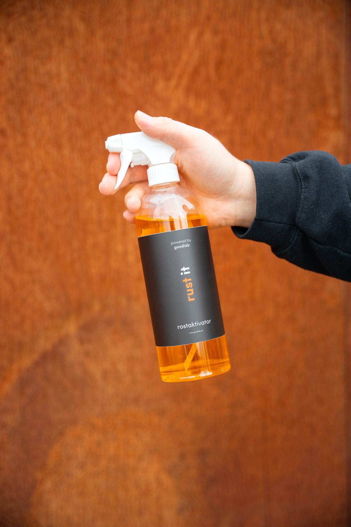 RustIT+ Rostaktivator-Flasche vor einer patinierten Corten-Oberfläche